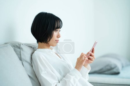 Photo for Woman sitting on sofa and using smartphone in the room - Royalty Free Image