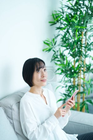 Foto de Mujer sentada en el sofá y usando el teléfono inteligente en la habitación - Imagen libre de derechos