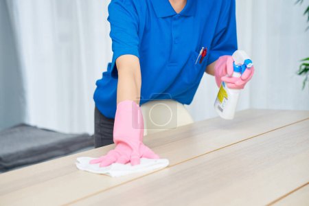 Foto de Una mujer con ropa de trabajo y máscara limpiando la habitación - Imagen libre de derechos