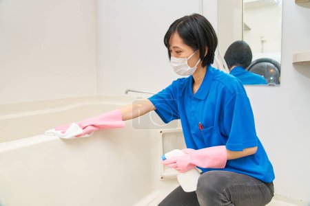 Téléchargez les photos : Une femme en vêtements de travail nettoie la salle de bain - en image libre de droit