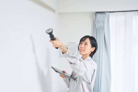 Téléchargez les photos : Une femme en vêtements de travail vérifiant l'état d'un mur de la maison - en image libre de droit