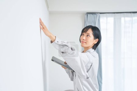 Photo for A woman in work clothes checking the condition of a house wall - Royalty Free Image