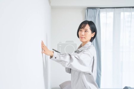 Téléchargez les photos : Une femme en vêtements de travail vérifiant l'état d'un mur de la maison - en image libre de droit