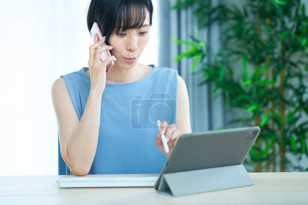 Téléchargez les photos : Femme faisant un appel téléphonique tout en regardant un écran d'ordinateur dans la chambre - en image libre de droit