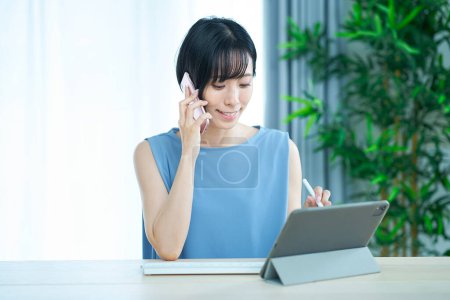 Foto de Mujer haciendo una llamada telefónica mientras mira la pantalla de una computadora en la habitación - Imagen libre de derechos