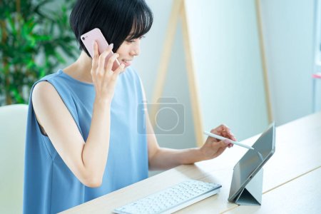 Foto de Mujer haciendo una llamada telefónica mientras mira la pantalla de una computadora en la habitación - Imagen libre de derechos