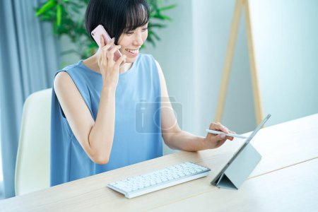Photo for Woman making a phone call while looking at a computer screen in the room - Royalty Free Image