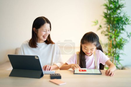 Téléchargez les photos : Une fille qui joue avec une femme qui travaille avec une tablette à la maison - en image libre de droit