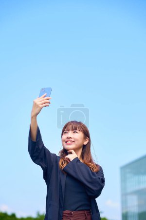 Photo for Young woman holding a smartphone under the blue sky - Royalty Free Image
