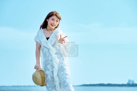 Photo for A young woman taking a commemorative photo at the beach on fine day - Royalty Free Image