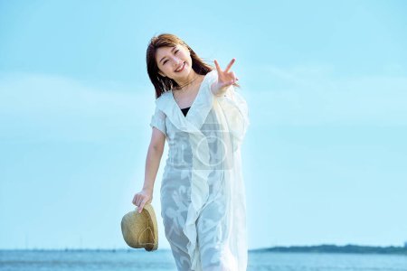 Photo for A young woman taking a commemorative photo at the beach on fine day - Royalty Free Image