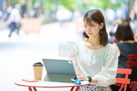Téléchargez les photos : Une femme opérant un PC à l'extérieur le beau jour - en image libre de droit