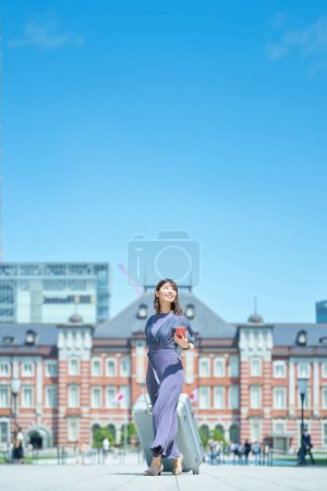 A woman walking in the city with a suitcase on fine day
