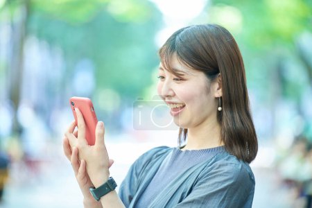 Téléchargez les photos : Jeune femme regardant l'écran du smartphone le beau jour - en image libre de droit