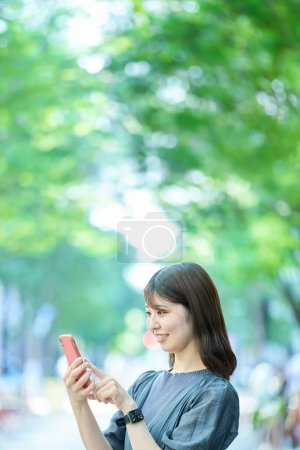 Téléchargez les photos : Jeune femme regardant l'écran du smartphone le beau jour - en image libre de droit