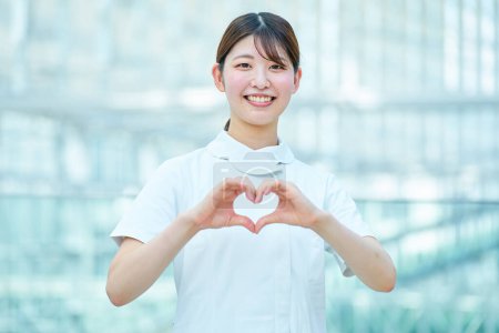 A woman in a white coat making a heart shape with both hands