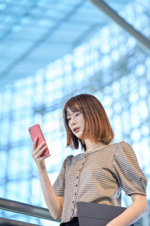 Téléchargez les photos : Asiatique jeune femme d'affaires opérant un smartphone - en image libre de droit