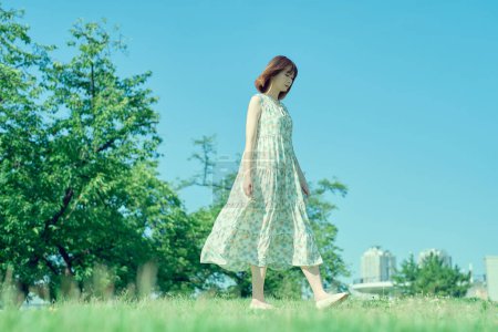 Téléchargez les photos : Jeune femme marchant dans un espace vert avec une expression détendue - en image libre de droit