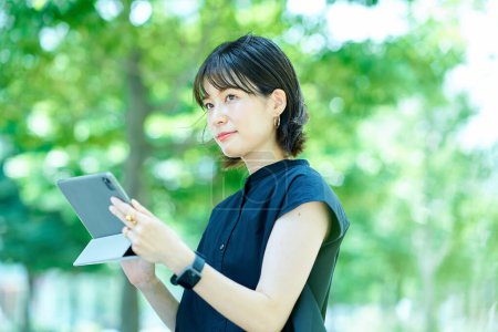Téléchargez les photos : Jeune femme opérant une tablette PC à l'extérieur - en image libre de droit