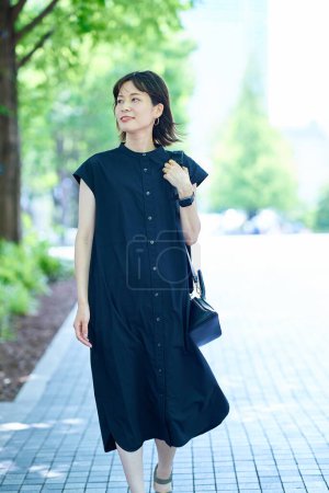 Photo for Young woman walking along a tree-lined street on fine day - Royalty Free Image