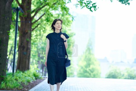Téléchargez les photos : Jeune femme marchant le long d'une rue bordée d'arbres le beau jour - en image libre de droit