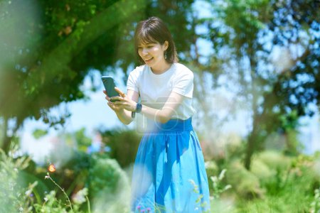 Téléchargez les photos : Une femme tenant un smartphone dans un espace vert le beau jour - en image libre de droit