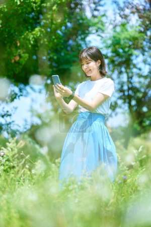 Photo for A woman holding a smartphone in a green space on fine day - Royalty Free Image