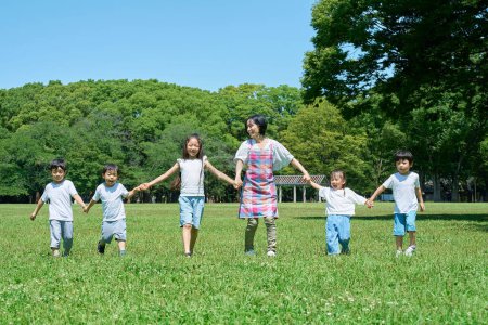 Photo for Woman in apron and children lined up holding hands in a green space - Royalty Free Image
