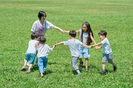 Photo for Children and woman holding hands and playing on the meadow - Royalty Free Image