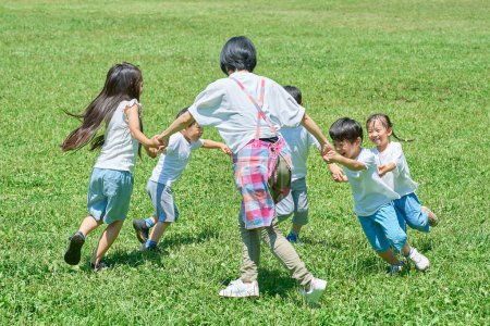 Foto de Niños y mujeres tomados de la mano y jugando en el prado - Imagen libre de derechos