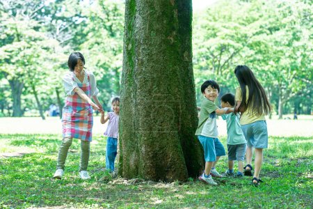 Téléchargez les photos : Enfants et femmes se tenant la main et contournant l'arbre dans le parc - en image libre de droit