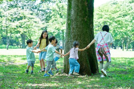 Photo for Children and woman holding hands and going around the tree in the park - Royalty Free Image