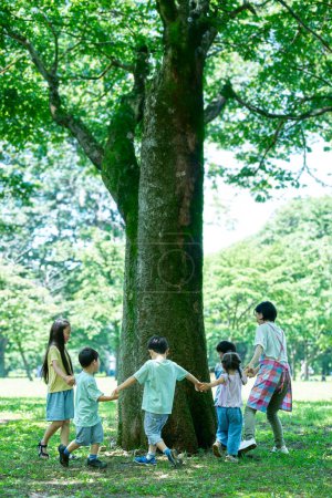 Téléchargez les photos : Enfants et femmes se tenant la main et contournant l'arbre dans le parc - en image libre de droit