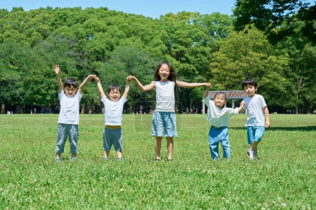 Téléchargez les photos : Les enfants tenant la main dans une rangée sur la prairie - en image libre de droit