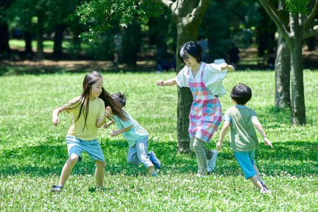 Téléchargez les photos : Une femme dans un tablier avec des enfants jouant à la chasse dans le parc - en image libre de droit