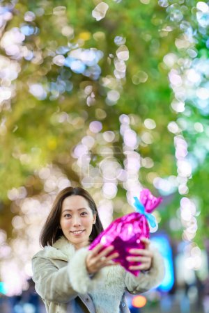 Photo for A woman holding a colorfully wrapped present outdoors at night - Royalty Free Image