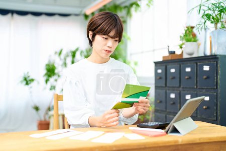 Photo for Young woman looking at her bankbook indoors - Royalty Free Image