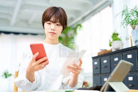 Téléchargez les photos : Une femme tenant une carte et opérant un smartphone dans la chambre - en image libre de droit