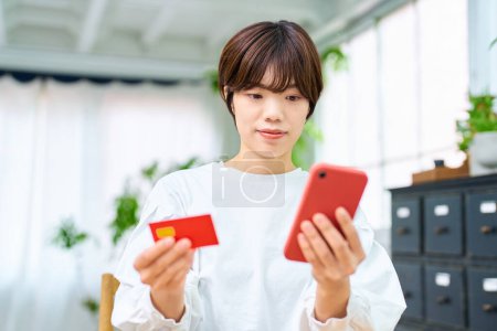 Foto de Una mujer sosteniendo una tarjeta y operando un teléfono inteligente en interiores - Imagen libre de derechos