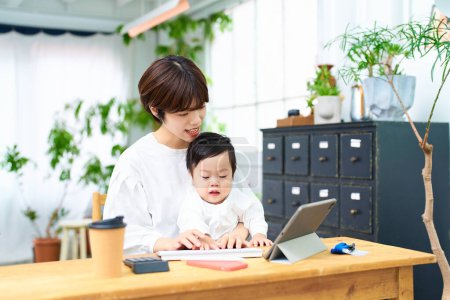 Foto de Una mujer sosteniendo a un bebé y operando una computadora en el interior - Imagen libre de derechos
