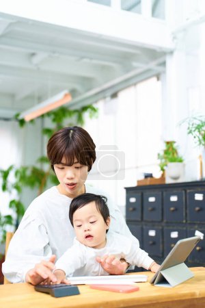 Téléchargez les photos : Une femme tenant un bébé et faisant fonctionner un ordinateur à l'intérieur - en image libre de droit