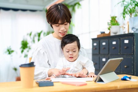 Foto de Una mujer sosteniendo a un bebé y operando una computadora en el interior - Imagen libre de derechos