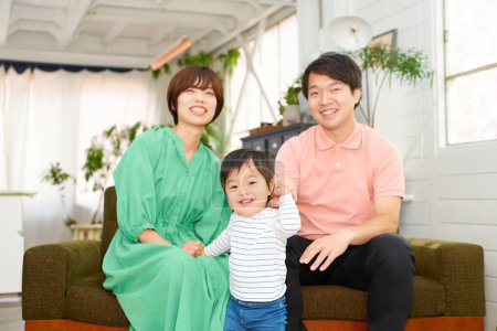 Téléchargez les photos : Une famille de trois souriants et relaxants à l'intérieur - en image libre de droit