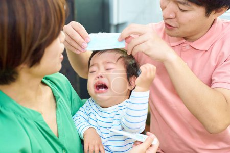 Téléchargez les photos : Parents réconfortant un bébé qui pleure et qui est malade - en image libre de droit