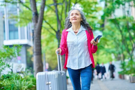 Téléchargez les photos : Femme âgée joyeuse se promenant dans la ville avec une valise - en image libre de droit