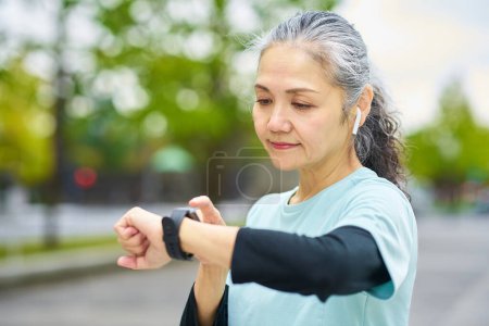 Photo for Senior woman operating a smartwatch outdoors - Royalty Free Image