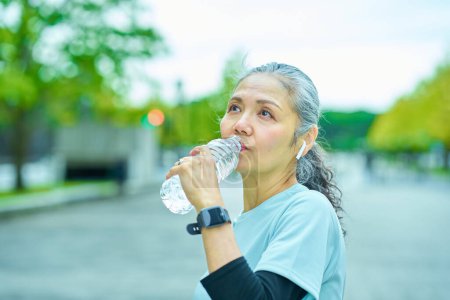 Téléchargez les photos : Femme âgée buvant de l'eau d'une bouteille en plastique à l'extérieur - en image libre de droit
