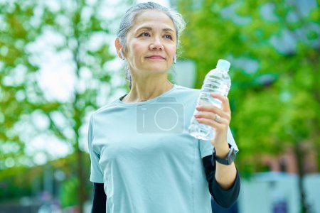 Téléchargez les photos : Femme âgée buvant de l'eau d'une bouteille en plastique à l'extérieur - en image libre de droit