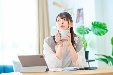 Téléchargez les photos : Jeune femme détendue prenant une pause avec une tasse tout en travaillant à la maison - en image libre de droit