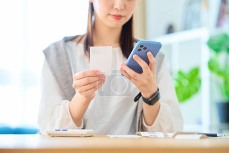 Photo for Young woman holding a receipt and smartphone in the room - Royalty Free Image